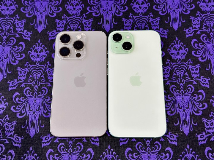 鬼屋壁纸餐垫上摆放着天然钛金属 iPhone 15 Pro（左）和绿色 iPhone 15。